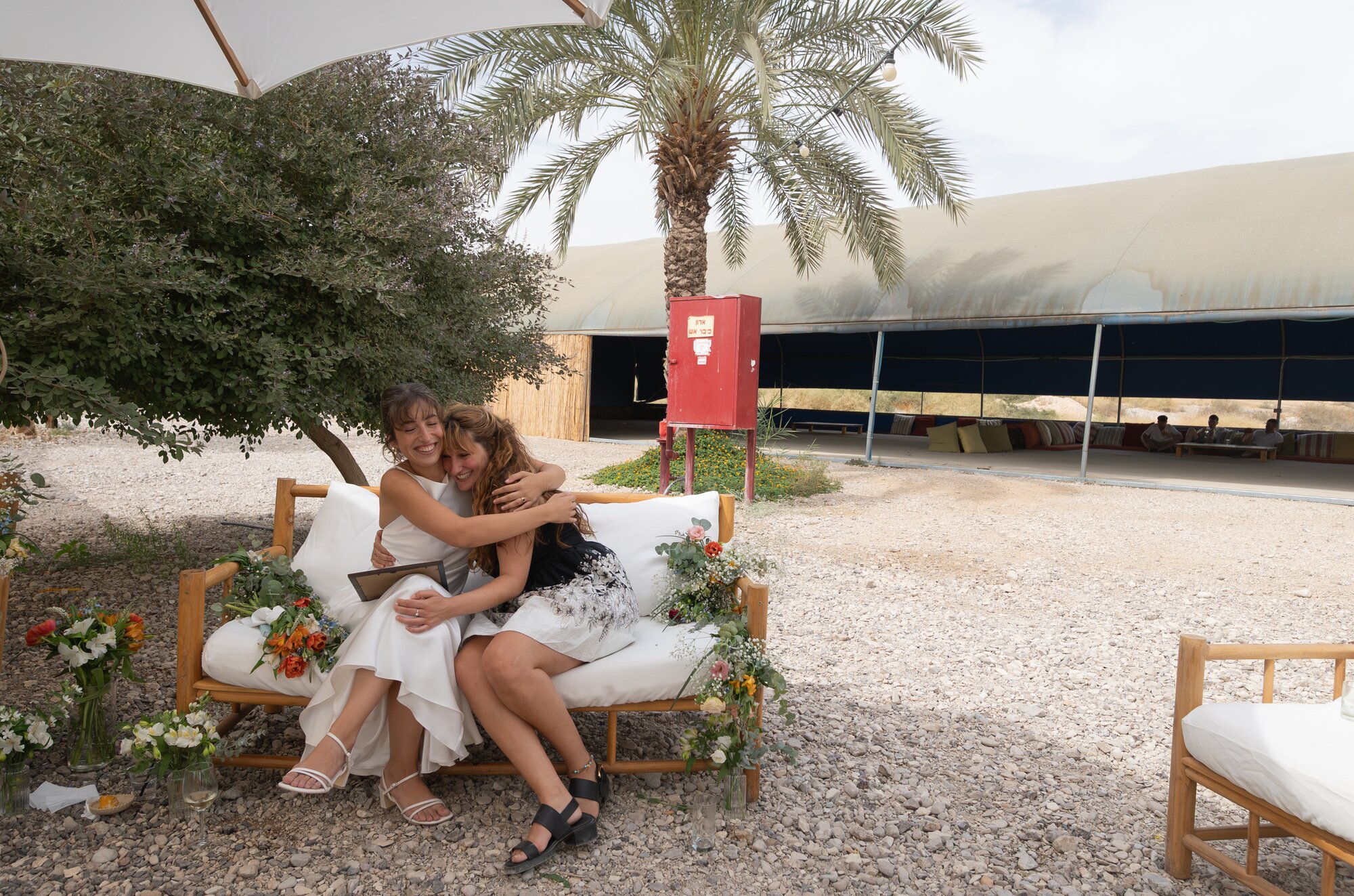 The bride embracing a friend on a garden sofa