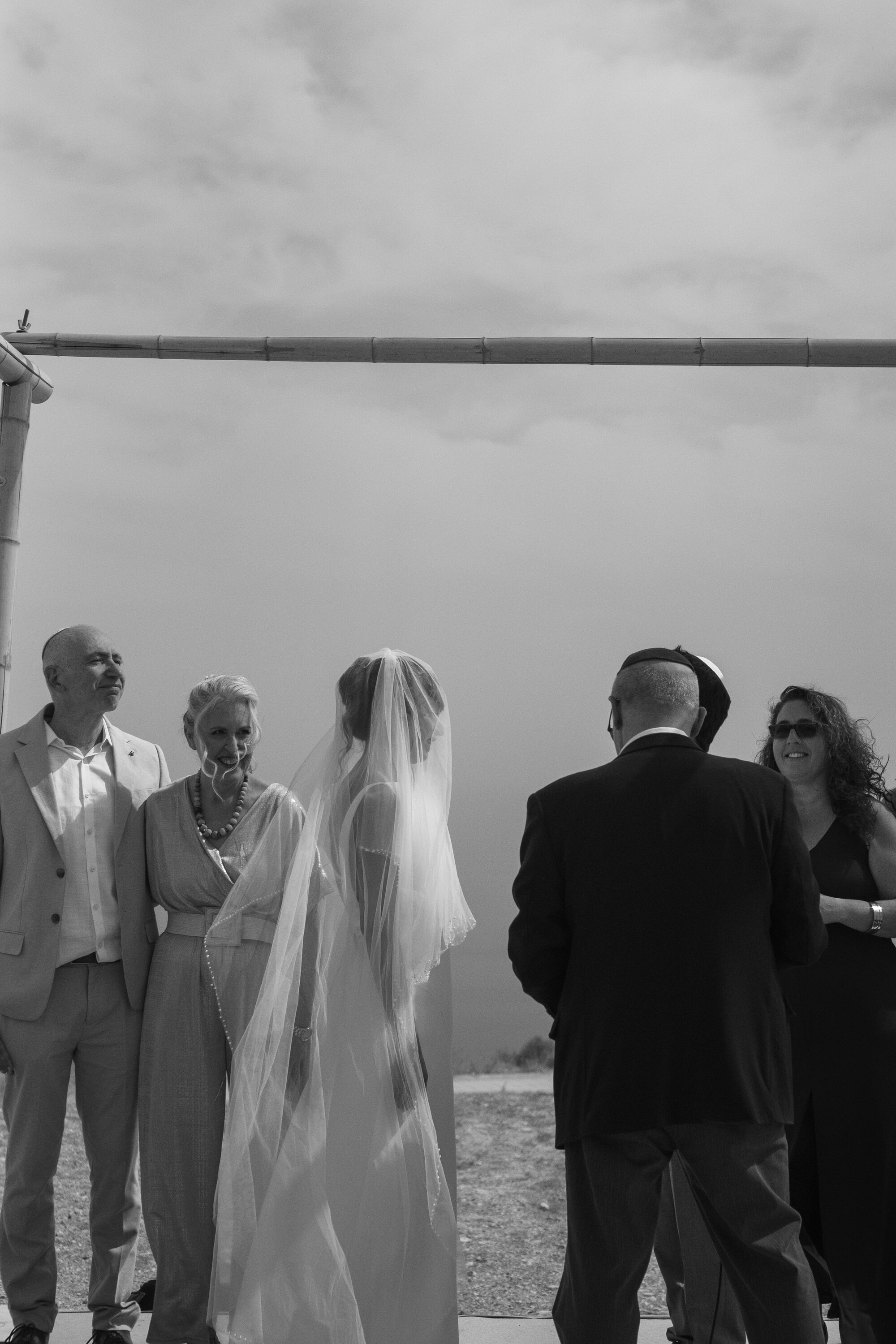 The bride, her parents and the rabbi under the chuppah, the sea beyond, black and white